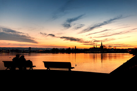 Sunset, Couple sitting on a bench, Lake Constance sea, in Konstanz, Germanyの写真素材