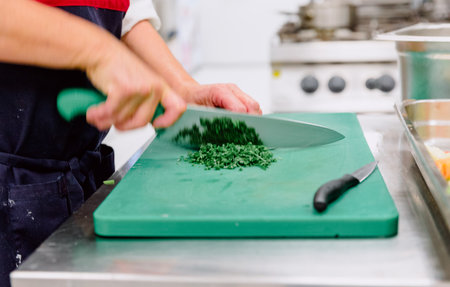 Unrecognized old woman cutting fresh parsley in a residence kitchen over a green table with two different knivesの写真素材