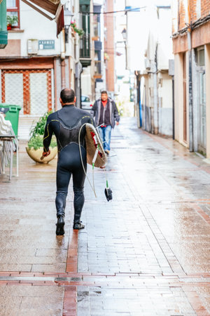 surfer walking down the street with wetsuit and surfboardの写真素材