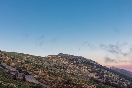 sunrise on a rocky mountain with green vegetation and blue sky with some cloudの写真素材
