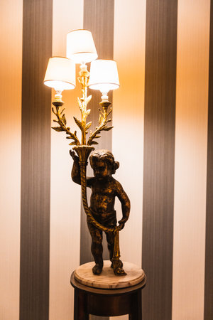 Lamp in the shape of a sculpture of a child holding the illuminated lights with a brown and white striped background.の写真素材