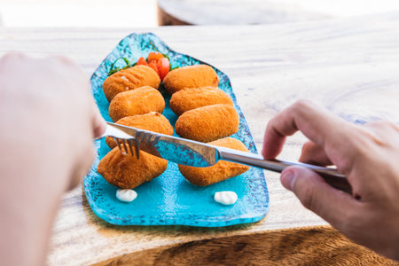 Hands cutting with knife and fork a plate of croquettes to eat.の写真素材