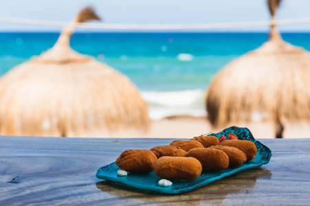Blue plate of croquettes in front of the beach with two umbrellas in the backgroundの写真素材