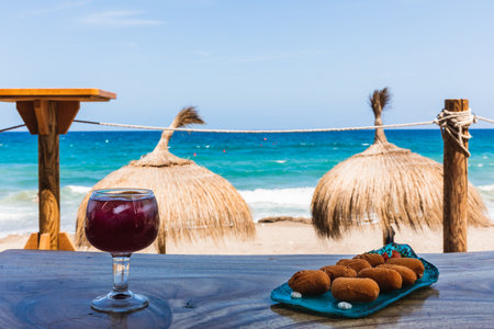 Glass of wine and plate of croquettes in front of the beach with two umbrellas in the backgroundの写真素材