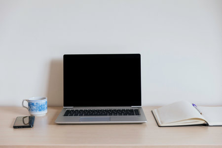 Workspace with black screen computer, open notepad, pen, coffee cup and smartphone. No people with...