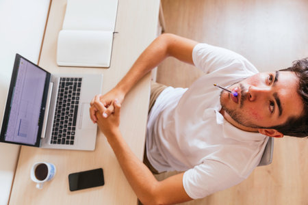 Young man sleeping on the table in front of the computer leaning on his arms, with a coffee, a smartphone and a notebook. Concept: teleworking or having online classesの写真素材