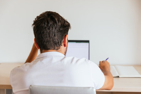 Young man sleeping on the table in front of the computer leaning on his arms, with a coffee, a...