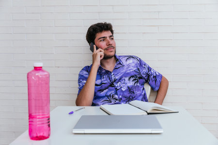 Young man talking on his smartphone looking at the horizon with blue hawaina shirt and white brick background. Concept: telework - cryptocurrencyの写真素材