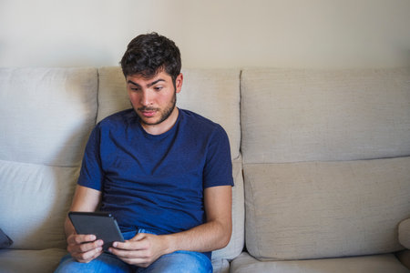 Young man surprised reading with his ebook on a sofaの写真素材