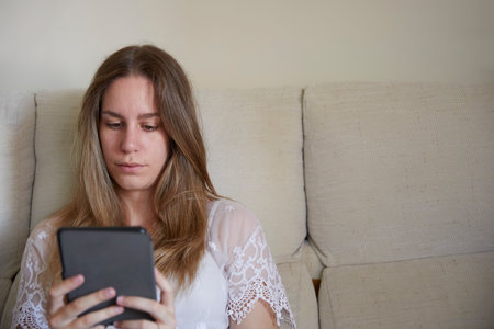 Young woman concentrating on reading with her ebook on a sofaの写真素材
