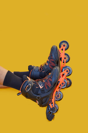 Two legs of a boy with inline skates one on top of the other on a yellow background with copyspace