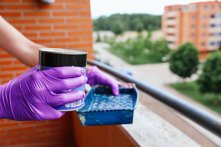 Unrecognizable woman's hands in purple gloves pouring paint from a can into a tray. Reformsの写真素材