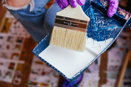 Unrecognizable woman's hands with purple gloves taking paint with a brush in a tray. Reformsの写真素材