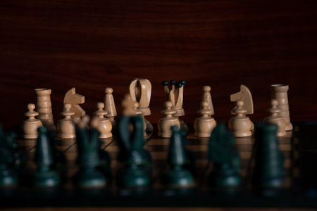 Chess board with white chess pieces in background and black chess pieces in foreground out of focus with wooden brown background. Concept: chessの写真素材