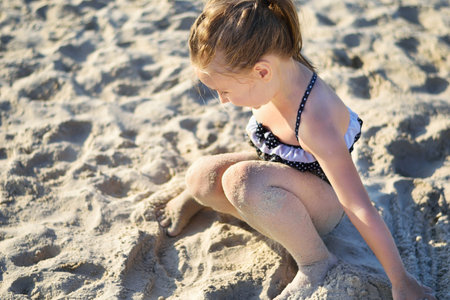 Adorable little girl playing with sand at the beach in summerの写真素材