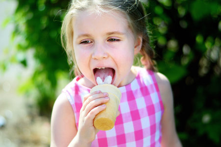 Adorable little girl eating tasty ice cream on summer dayの写真素材