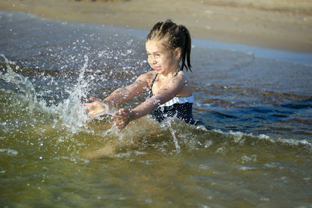 Adorable little girl is splashing and smashing sea water and having funの写真素材