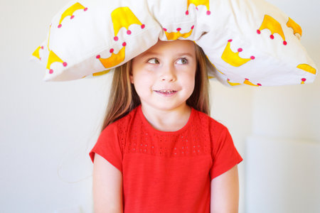 Adorable little girl playing with the pillow on the bed in her bedroomの写真素材