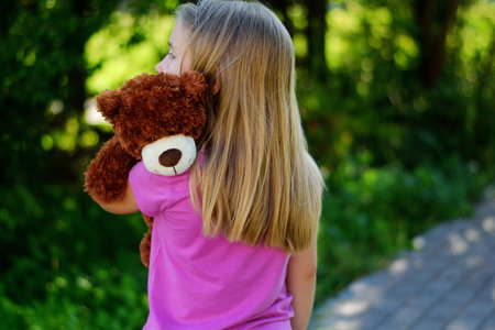 Adorable sad girl with teddy bear in parkの写真素材