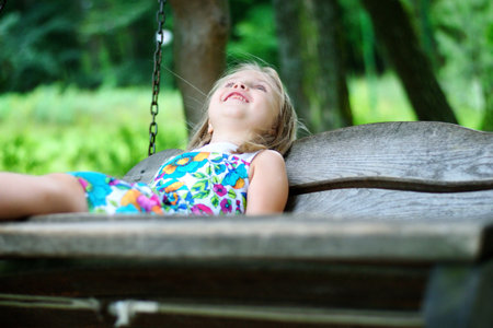 Adorable girl having fun on a wooden swing on summer dayの写真素材