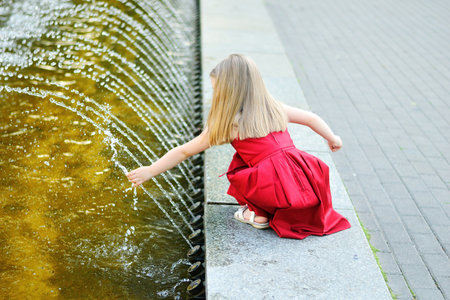 Cute little girl playing with a city fountain on hot and sunny summer dayの写真素材