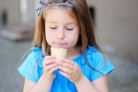 Adorable little girl eating tasty ice cream at park on sunny summer dayの写真素材
