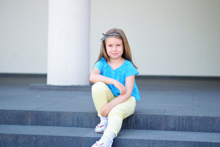 Adorable little beautiful girl sitting on a stairway outdoorの写真素材