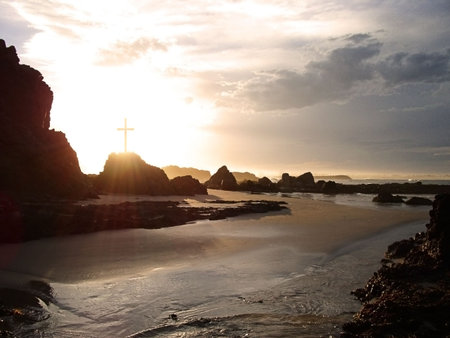 Rays of light pass through a crucifix on a rocky coastlineの写真素材