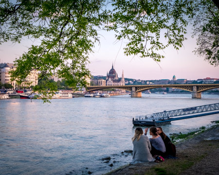 Three girls are sitting on the banks of the Danube in a park on Margaret Island.のeditorial素材