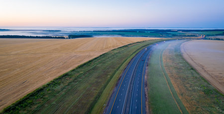 Highway along the wheat fields at dawn. Morning landscape from a height.