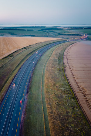 Highway going through meadow in mist surrounded by forest. Aerial view of a road covered in fog.