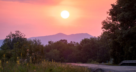 the sun rises against the background of the mountains. Green grass and a road stretching into the distance. Stanitsa Dakhovskaya, Republic of Adygea, Russia.の写真素材