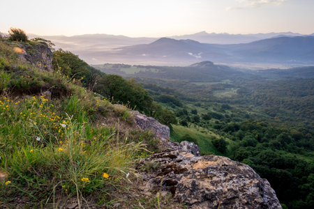 Early morning just after sunrise. Silhouettes of mountains in the morning haze, grass and wildflowers in the foreground. Alpine summer landscape. Lagonaki Plateau, Republic of Adygea, Russiaの写真素材
