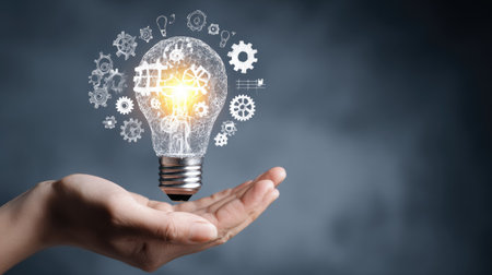 A creative representation of a hand holding a glowing light bulb surrounded by gears, symbolizing innovation and the generation of new ideas in technology.の素材