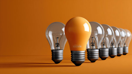 This visually striking image features a bold orange light bulb distinctively placed among clear bulbs on a vibrant orange background, emphasizing creativity and innovation.の素材