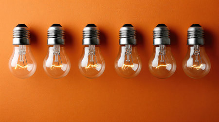 A striking image of six classic light bulbs with glowing filaments set against a vibrant orange backdrop. Perfect for adding warmth and creativity to your projects.の素材