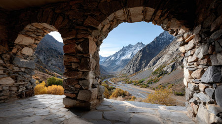 Explore a breathtaking view of a remote mountain valley framed by an ancient stone archway, showcasing stunning autumn colors and majestic peaks.の素材