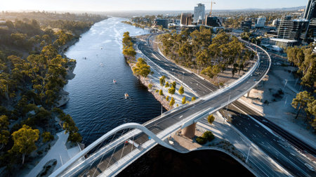 A stunning aerial view showcasing a sleek, curved bridge over a serene river. Surrounded by lush trees and modern buildings, this picturesque scene captures the essence of urban beauty and tranquility.の素材