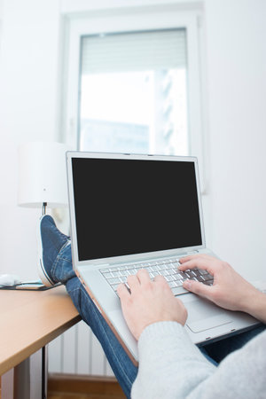 Businessman sitting relaxed and working on his computer with legs upの写真素材