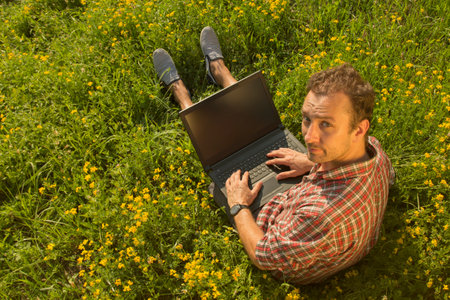 Young man sitting in the meadow with his laptop
