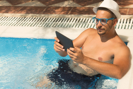 Man using tablet device while relaxing in the hydro massage part of the swimming pool の写真素材