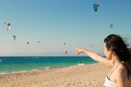 Young woman points the finger at kitesurfing kites on the beachの写真素材