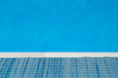 Blue bamboo straw mat ideal for product placement. Blue swimming pool water surface and white swimming pool edge in the background.  の写真素材