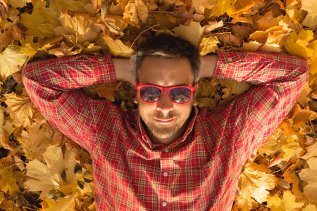 Young guy lying on yellow leaves covered ground and enjoying the autumn season. Top down viewpoint.の写真素材