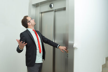 Businessman pressing the elevator up button and looking the elevator display that indicates that elevator stopped working.   の写真素材