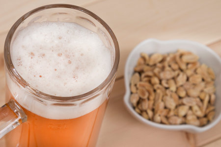 Mug of beer and peanuts in the bowl in the background. の写真素材
