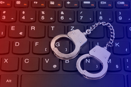 Cybercriminal concept. Keychain handcuffs on the computer keyboard. Police lights luminosity.   