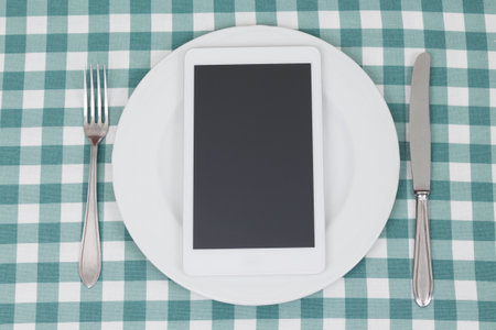 White digital tablet device in plate, knife and fork on the tablecloth. Top down viewpoint. の写真素材