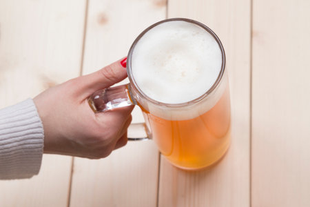 Top down viewpoint of female hand holding mug of beer on the table.の写真素材