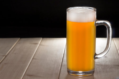 Mug of unfiltered beer on the wooden table. Backlight. Black background ideal for adding the...